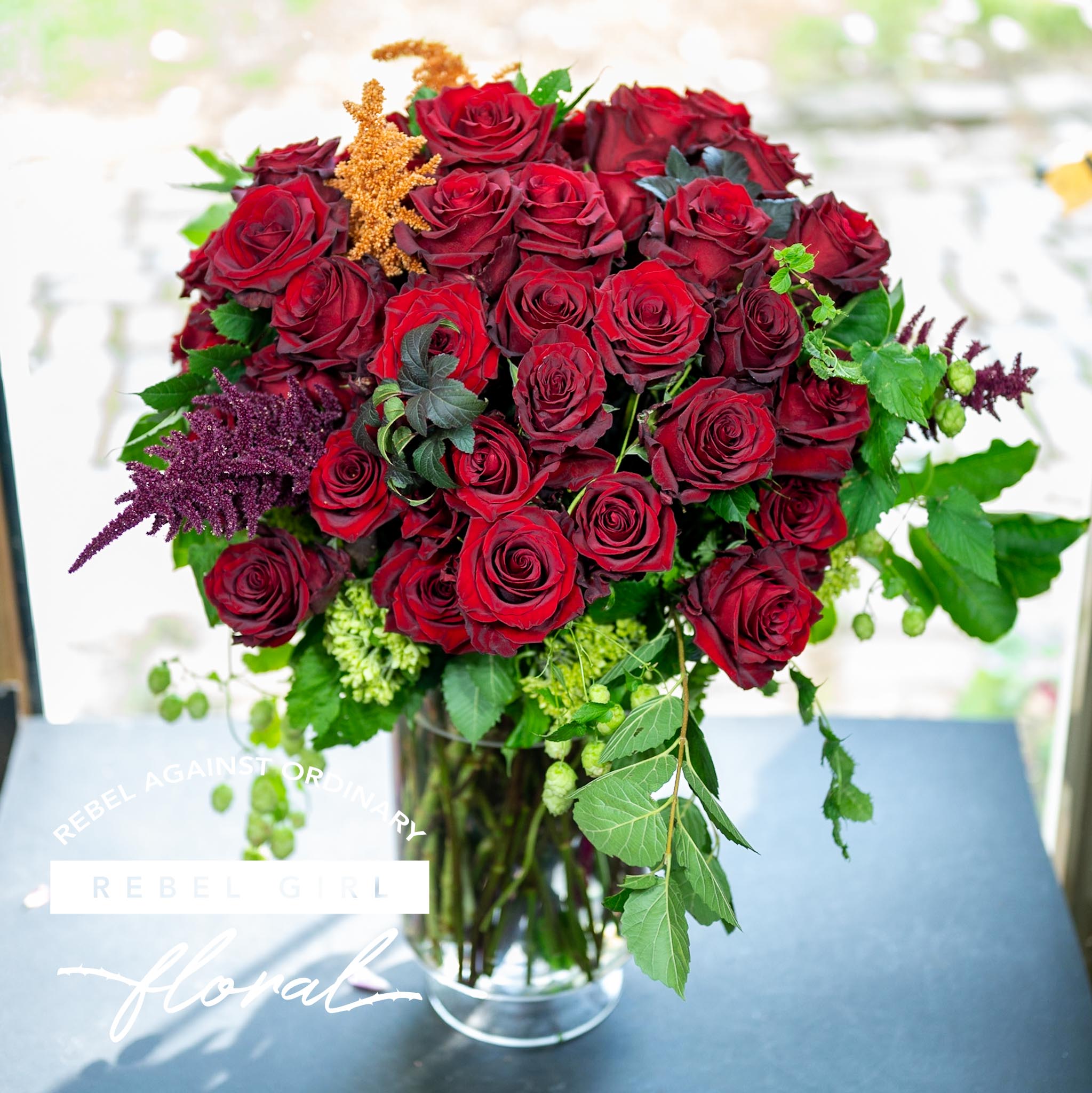 Beautiful bouquet of red roses with unique greens and accents arranged by Rebel Girl Floral